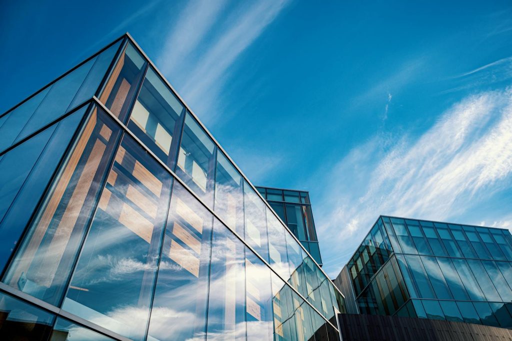 Vue en contre-plongée d'immeubles de bureaux contemporains en verre reflétant un ciel d'un bleu éclatant.