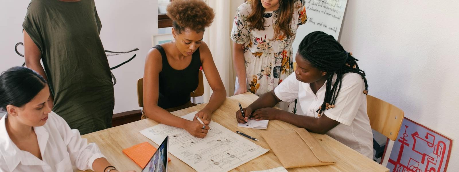 Une équipe diversifiée collabore à un projet en utilisant des ressources numériques et papier dans un bureau lumineux.